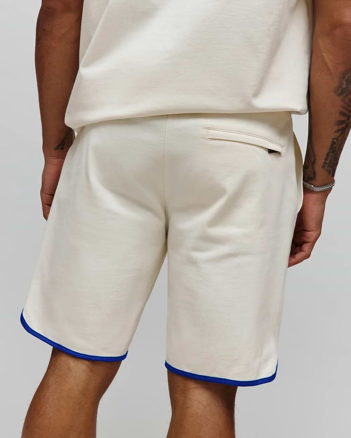 Mens Toby Short in cream, a relaxed fit short crafted from soft jersey, featuring distinctive blue piping along the hem and a discreet back welt pocket. (3)