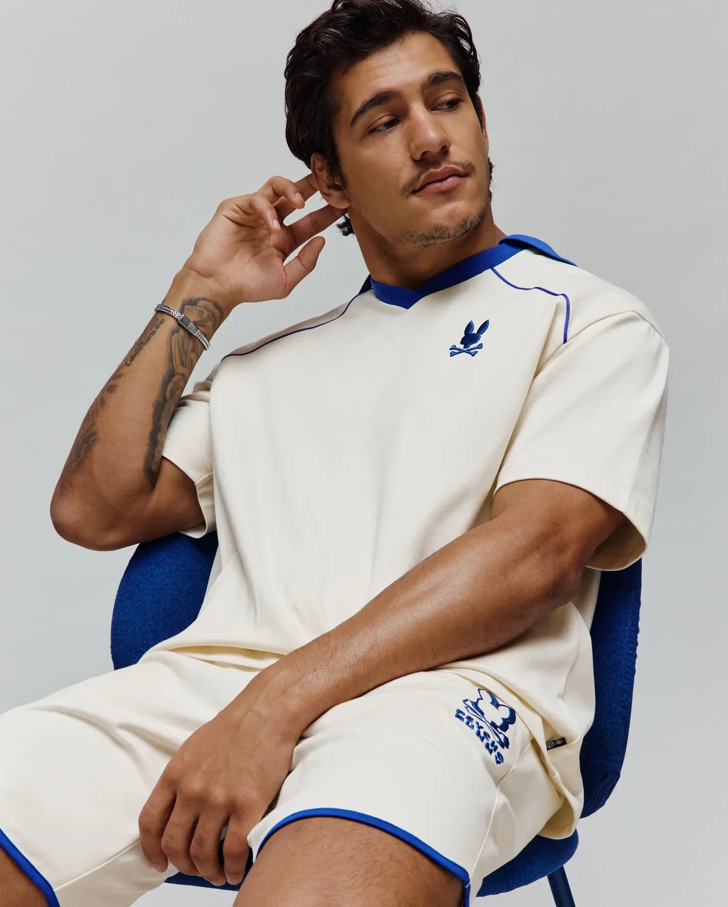 Cream relaxed-fit jersey T-shirt with royal blue V-neck trim and shoulder piping, featuring a small embroidered Psycho Bunny skull logo. Matching Mens Toby Short with blue piping and large embroidered Psycho Bunny logo. (4)