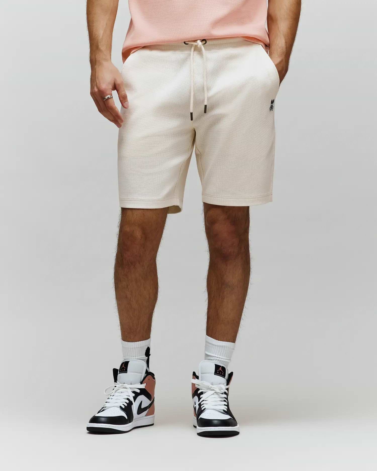 Mens Maxton Waffle Sweatshort in cream, featuring a relaxed fit, waffle knit texture, drawstring waist with black tips, and a small embroidered black Psycho Bunny skull logo on the left thigh.
