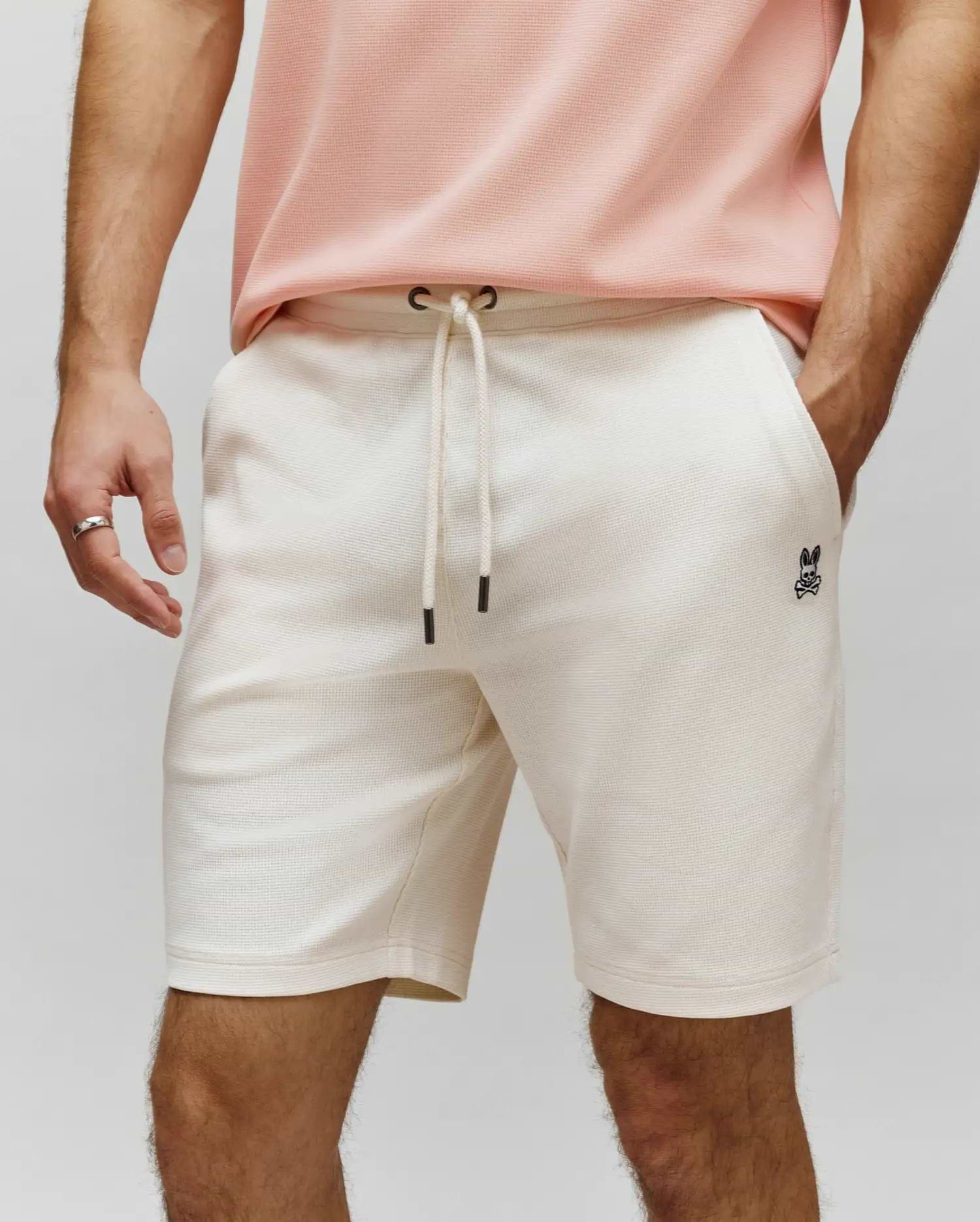 Mens Maxton Waffle Sweatshort in cream, featuring a relaxed fit, waffle knit texture, drawstring waist with black tips, and a small embroidered black Psycho Bunny skull logo on the left thigh.
