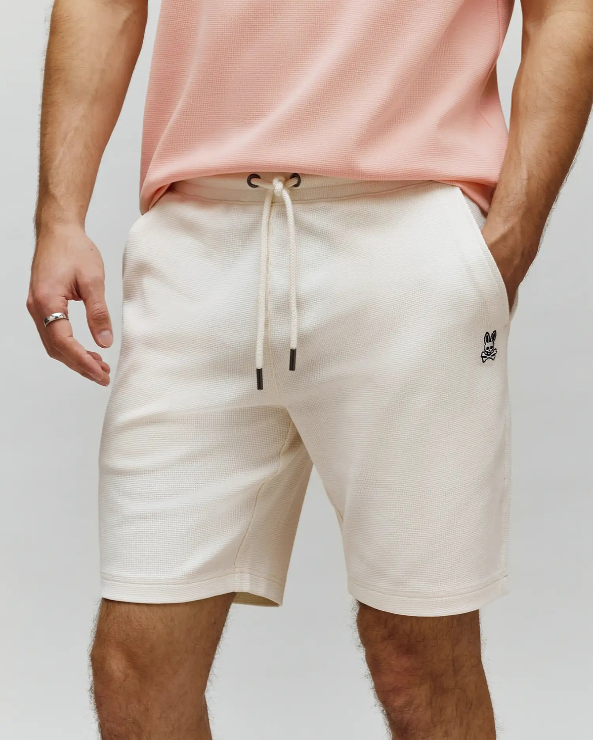 Mens Maxton Waffle Sweatshort in cream, featuring a relaxed fit, waffle knit texture, drawstring waist with black tips, and a small embroidered black Psycho Bunny skull logo on the left thigh.