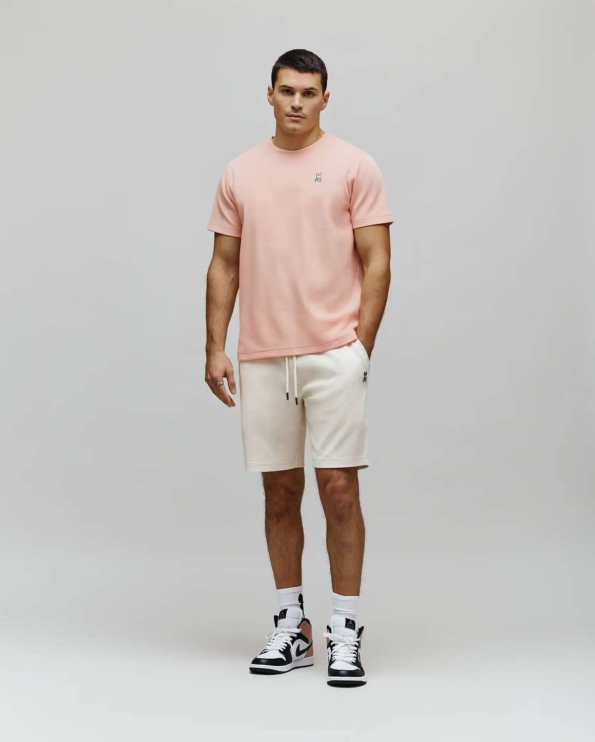 Peach textured t-shirt with a small embroidered Psycho Bunny skull logo on the left chest, paired with cream Mens Maxton Waffle Sweatshort featuring a drawstring waist and a small embroidered Psycho Bunny logo on the left thigh.