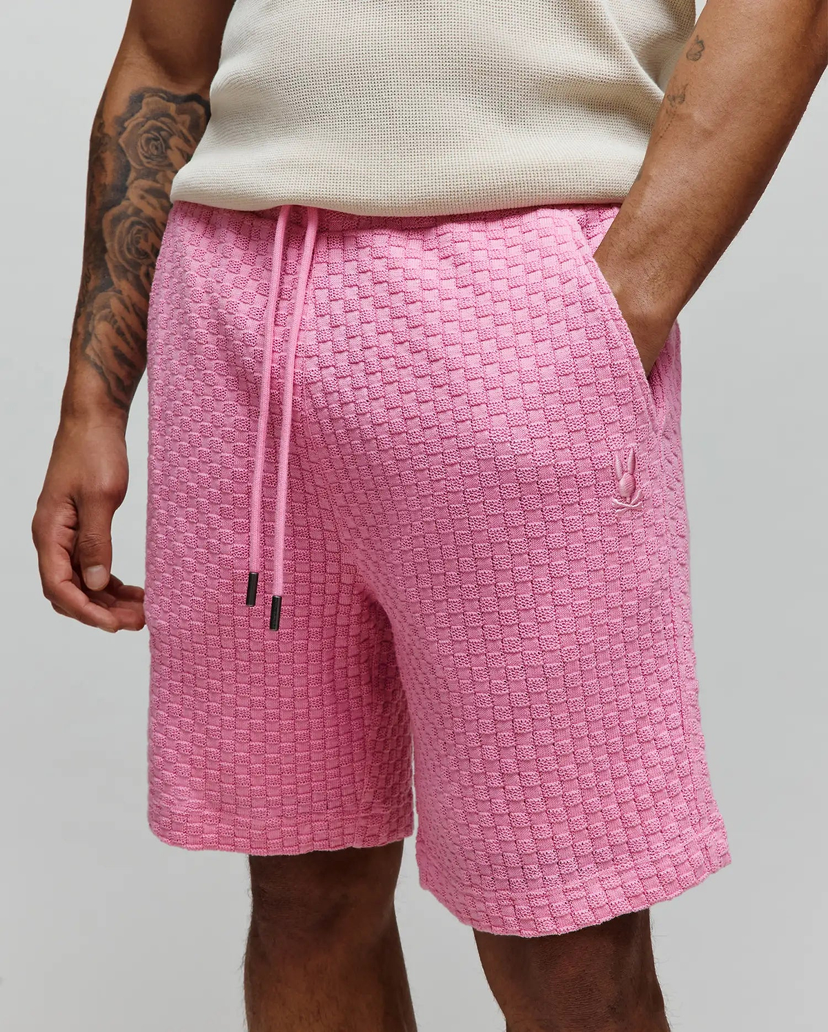 Mens Garen Knit Short, a relaxed fit pink knit short featuring a prominent woven checkerboard texture, a drawstring waist with black tips, and a small embroidered Psycho Bunny skull logo on the right thigh. (2)