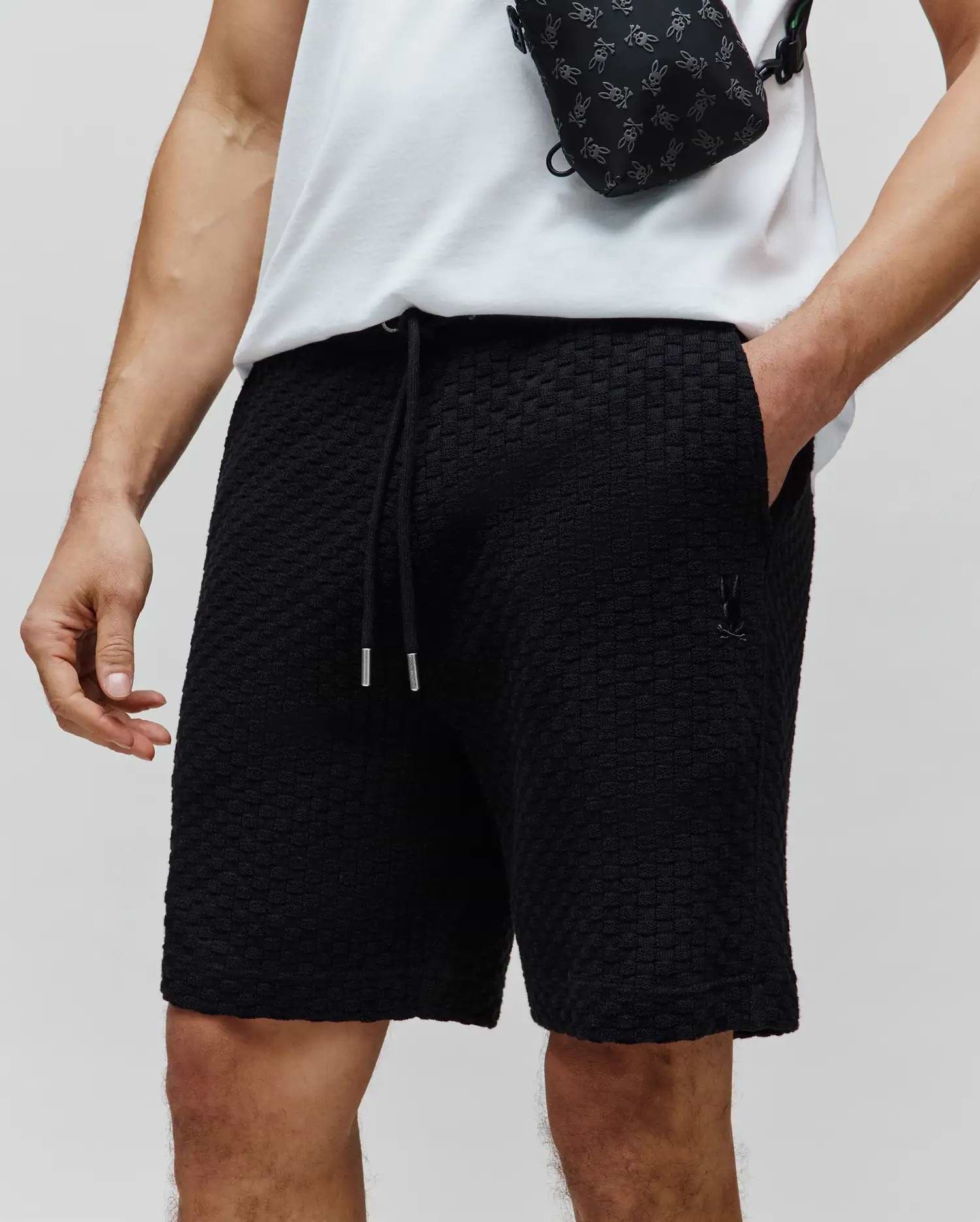 Mens Garen Knit Short, black textured knit fabric, relaxed fit, with a drawstring waist featuring silver tips and a small embroidered black Psycho Bunny skull logo on the left thigh. (2)
