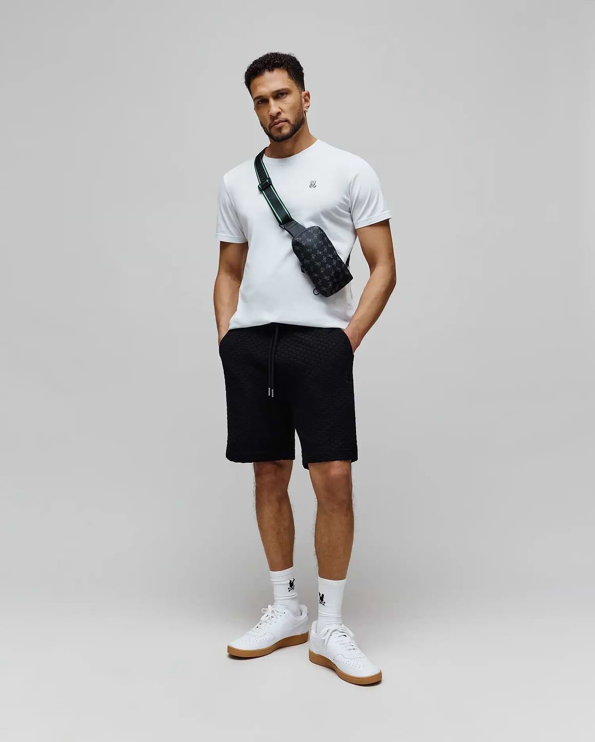 White classic fit jersey t-shirt with small embroidered Psycho Bunny logo on left chest, paired with black Mens Garen Knit Short featuring an all-over textured knit pattern and drawstring waist with silver tips. (4)