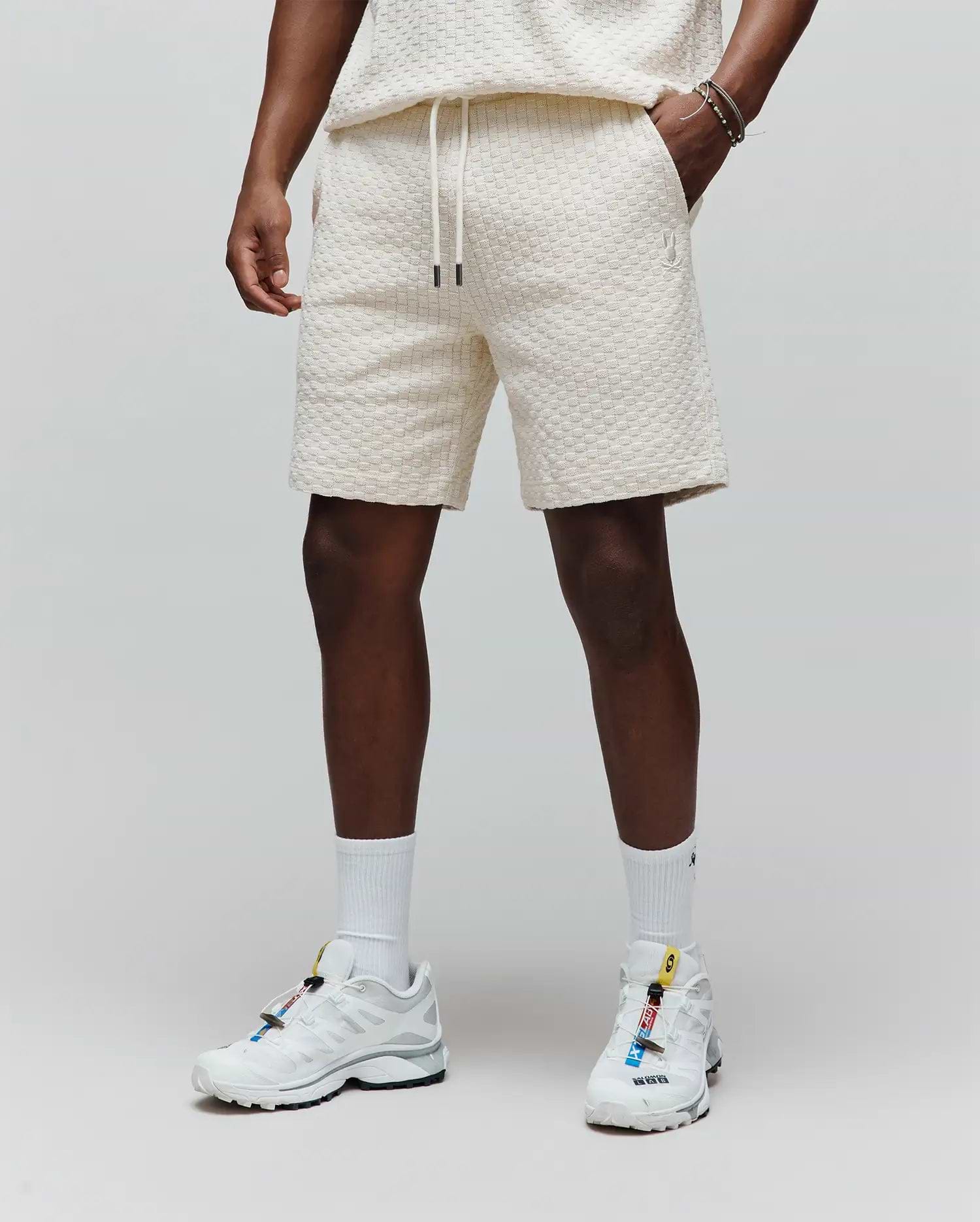 Mens Garen Knit Short, a cream relaxed-fit short with a textured waffle knit, drawstring waist with black tips, and a small embroidered Psycho Bunny logo on the left thigh. (1)