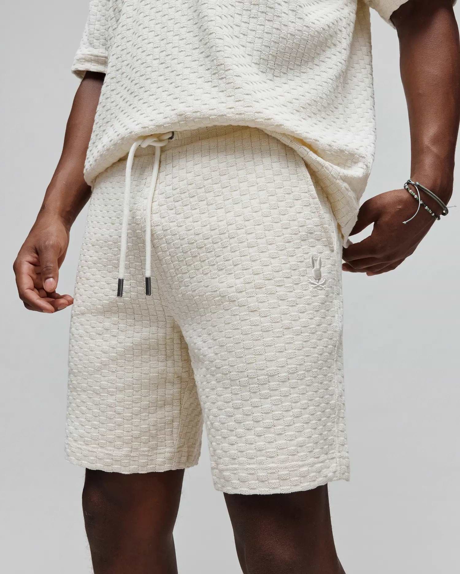 Mens Garen Knit Short in ecru, a relaxed fit short with a textured checkered knit, drawstring waist featuring dark tips, and a small embroidered Psycho Bunny skull logo on the left thigh. (2)