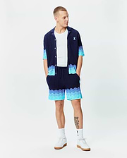Navy blue knit short-sleeve shirt and Mens Holden Knit Short 6, featuring a wavy knit texture with light blue to turquoise gradient accents, and small embroidered Psycho Bunny logos on the chest and right thigh.