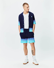 Navy blue knit short-sleeve shirt and Mens Holden Knit Short 6, featuring a wavy knit texture with light blue to turquoise gradient accents, and small embroidered Psycho Bunny logos on the chest and right thigh.
