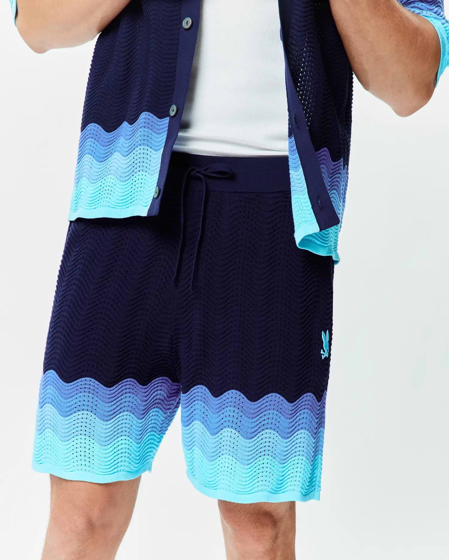Mens Holden Knit Short in navy with a wavy knit texture, featuring light blue and purple-blue wave patterns at the hem, and a small embroidered Psycho Bunny logo on the left thigh.