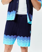 Mens Holden Knit Short in navy with a wavy knit texture, featuring light blue and purple-blue wave patterns at the hem, and a small embroidered Psycho Bunny logo on the left thigh.