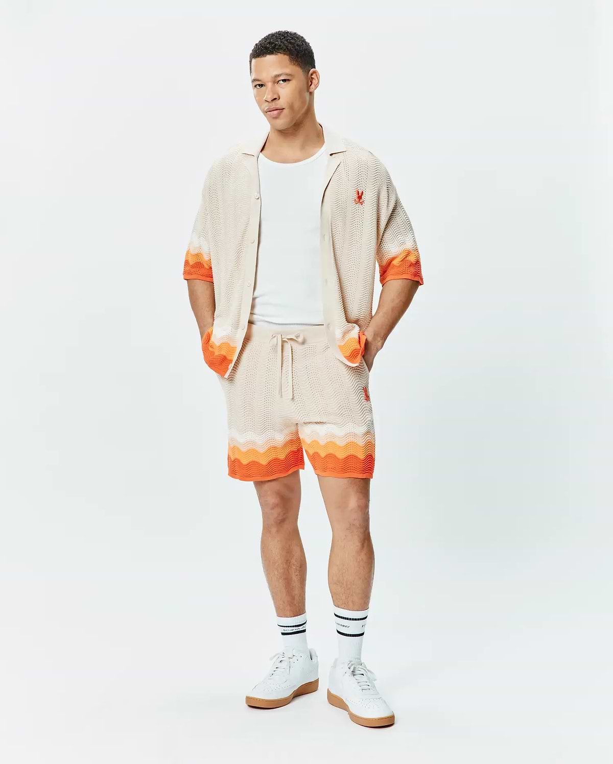 Beige knit short-sleeve shirt and matching Mens Holden Knit Short 6 set, featuring a wavy texture, vibrant orange accents, and small red embroidered Psycho Bunny skull logos.