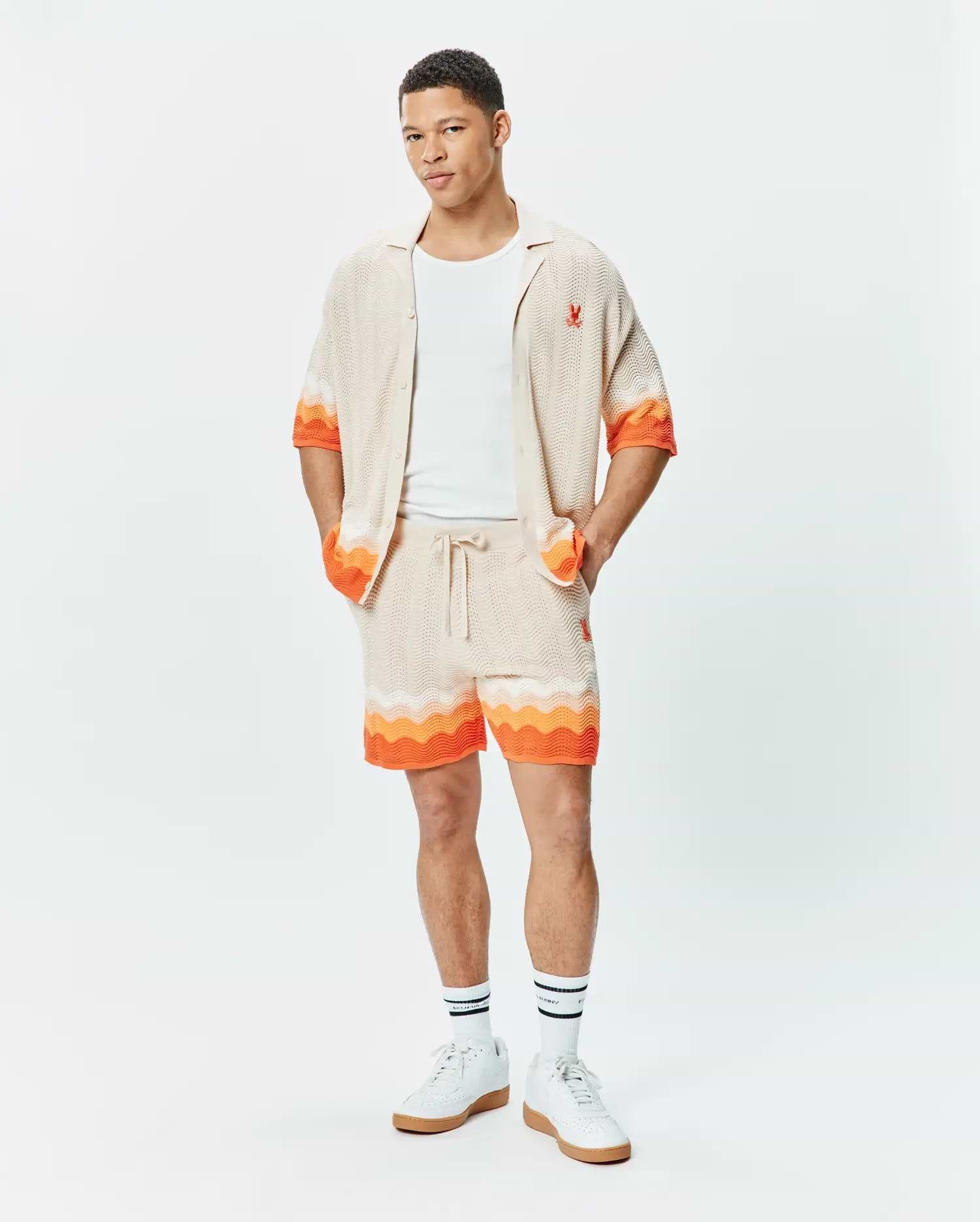 Beige knit short-sleeve shirt and matching Mens Holden Knit Short 6 set, featuring a wavy texture, vibrant orange accents, and small red embroidered Psycho Bunny skull logos.