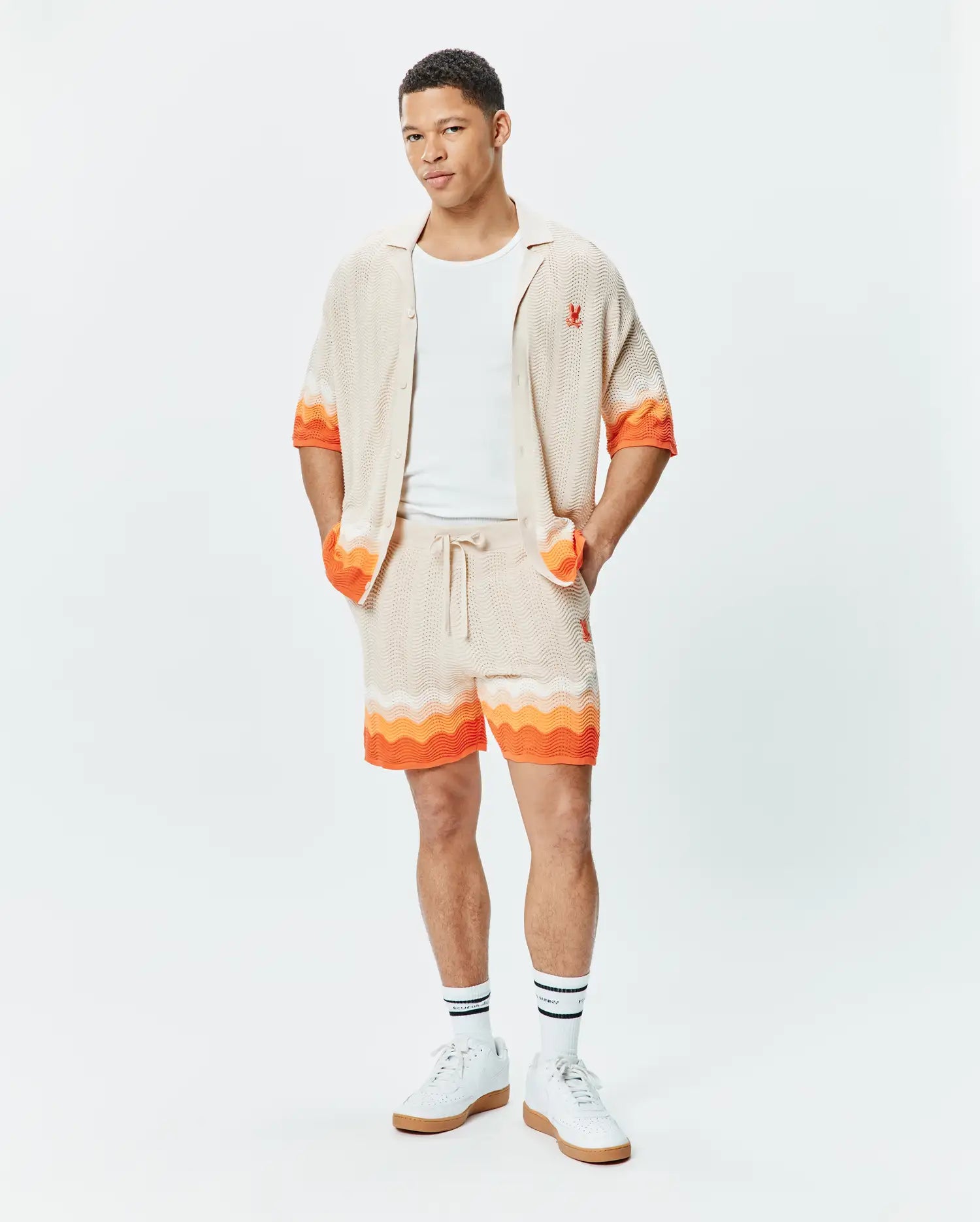 Beige knit short-sleeve shirt and matching Mens Holden Knit Short 6 set, featuring a wavy texture, vibrant orange accents, and small red embroidered Psycho Bunny skull logos.
