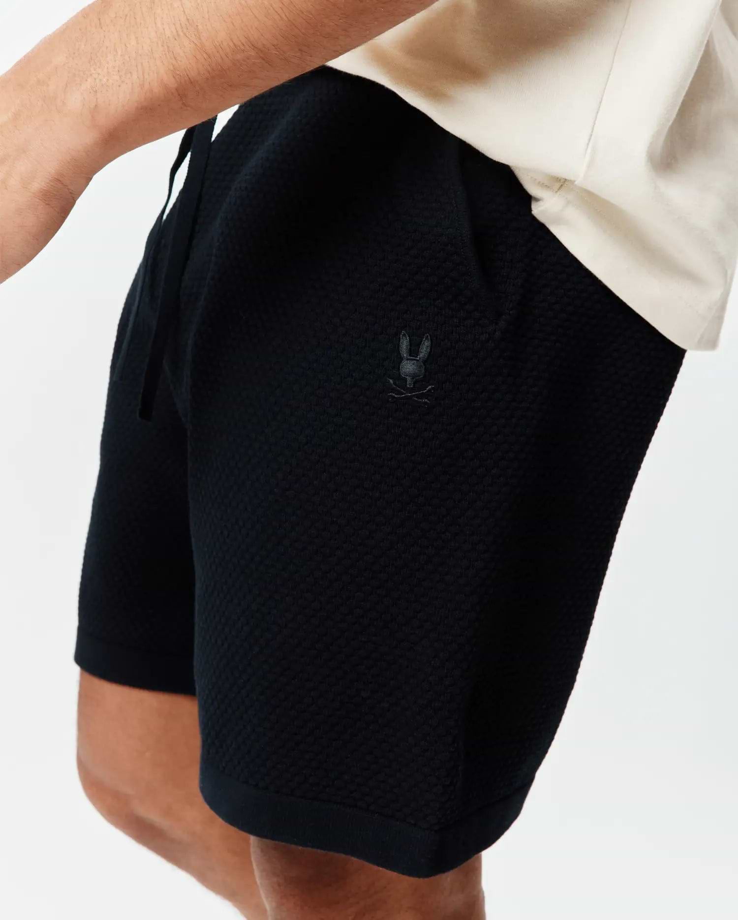 Psycho Bunny Black Mens Devon Knit Short, a relaxed fit with textured knit fabric, drawstring waist, and small tonal embroidered bunny skull logo on the left thigh.