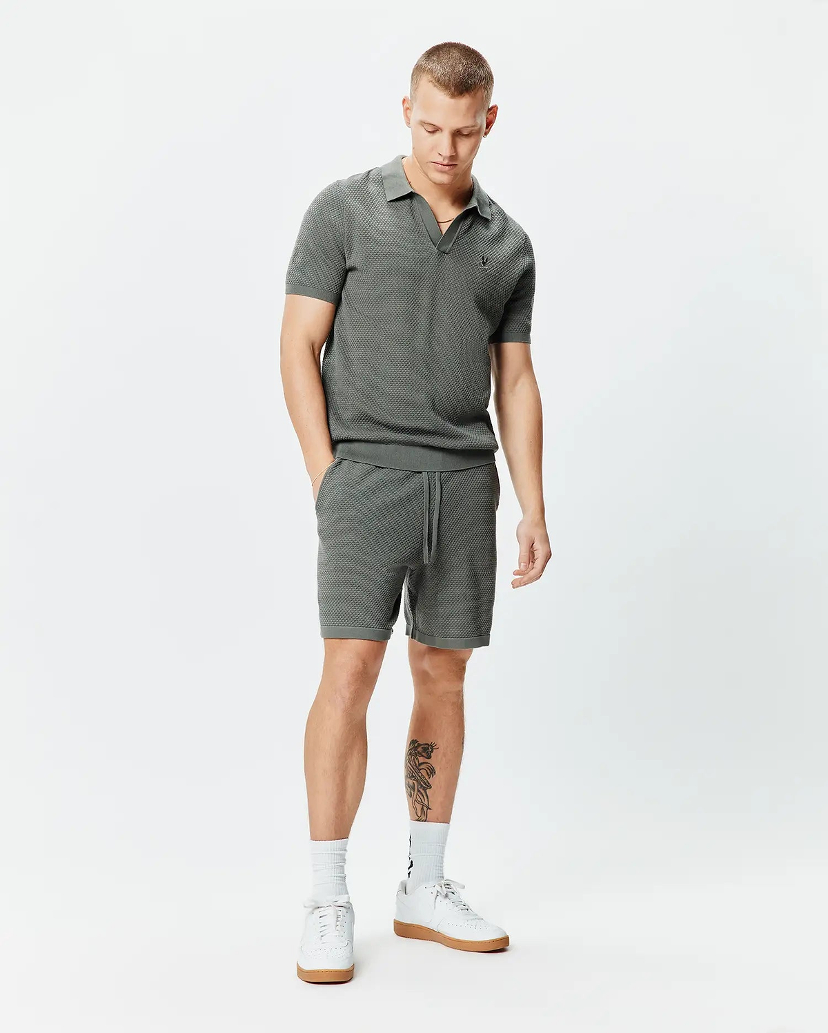Dark grey textured knit polo with open collar and small embroidered Psycho Bunny skull logo on left chest, paired with matching Mens Devon Knit Short 7 featuring a drawstring waist and 7-inch inseam, both in a classic fit.