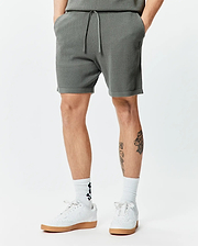 Mens Devon Knit Short 7, a dark grey textured knit short with a relaxed fit, features a drawstring waist and a small embroidered Psycho Bunny skull logo on the left thigh.