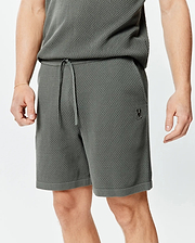 Mens Devon Knit Short 7, a relaxed fit charcoal textured knit short featuring a drawstring waist, ribbed hem, and a small embroidered Psycho Bunny skull logo on the left thigh.