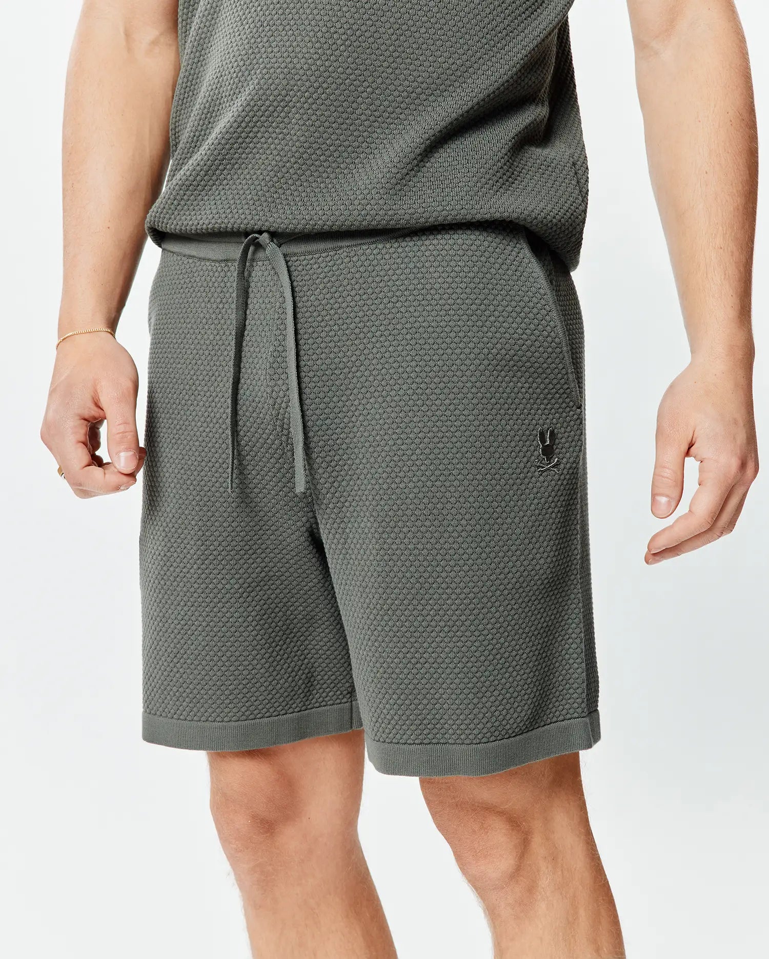 Mens Devon Knit Short 7, a relaxed fit charcoal textured knit short featuring a drawstring waist, ribbed hem, and a small embroidered Psycho Bunny skull logo on the left thigh.