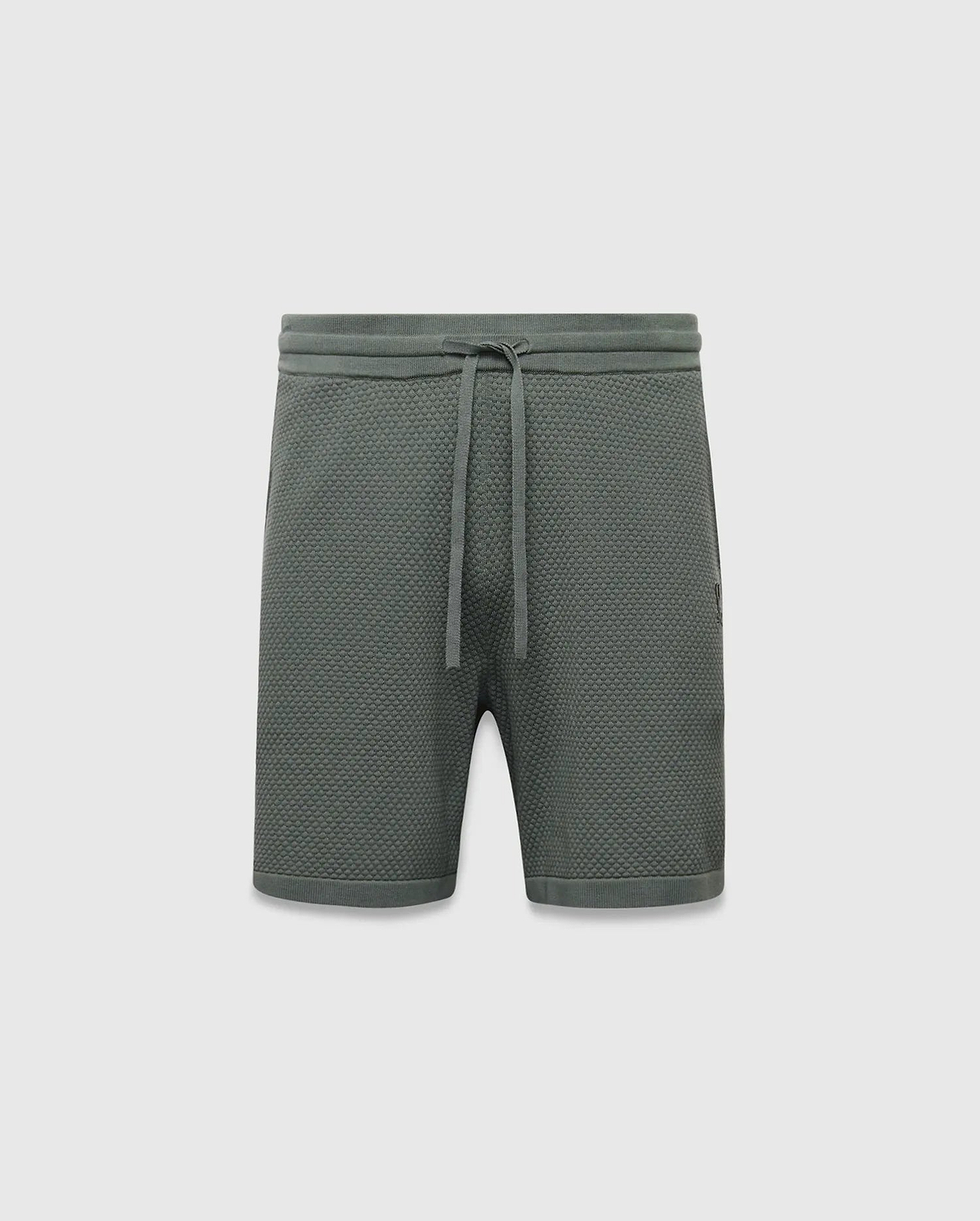 Mens Devon Knit Short 7, a relaxed fit dark green short featuring a textured pique knit fabric, drawstring waist, and a small tonal embroidered Psycho Bunny skull logo on the right leg.