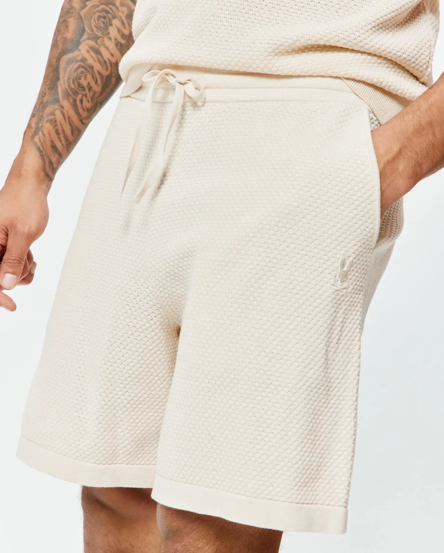 Mens Devon Knit Short, cream textured knit shorts with a relaxed fit, drawstring waist, and small tonal embroidered Psycho Bunny skull logo on the left thigh.