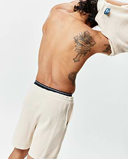 Cream Mens Devon Knit Short, a relaxed waffle knit short with a black and white striped waistband, paired with a matching cream waffle knit top featuring a blue Psycho Bunny tag at the back collar.