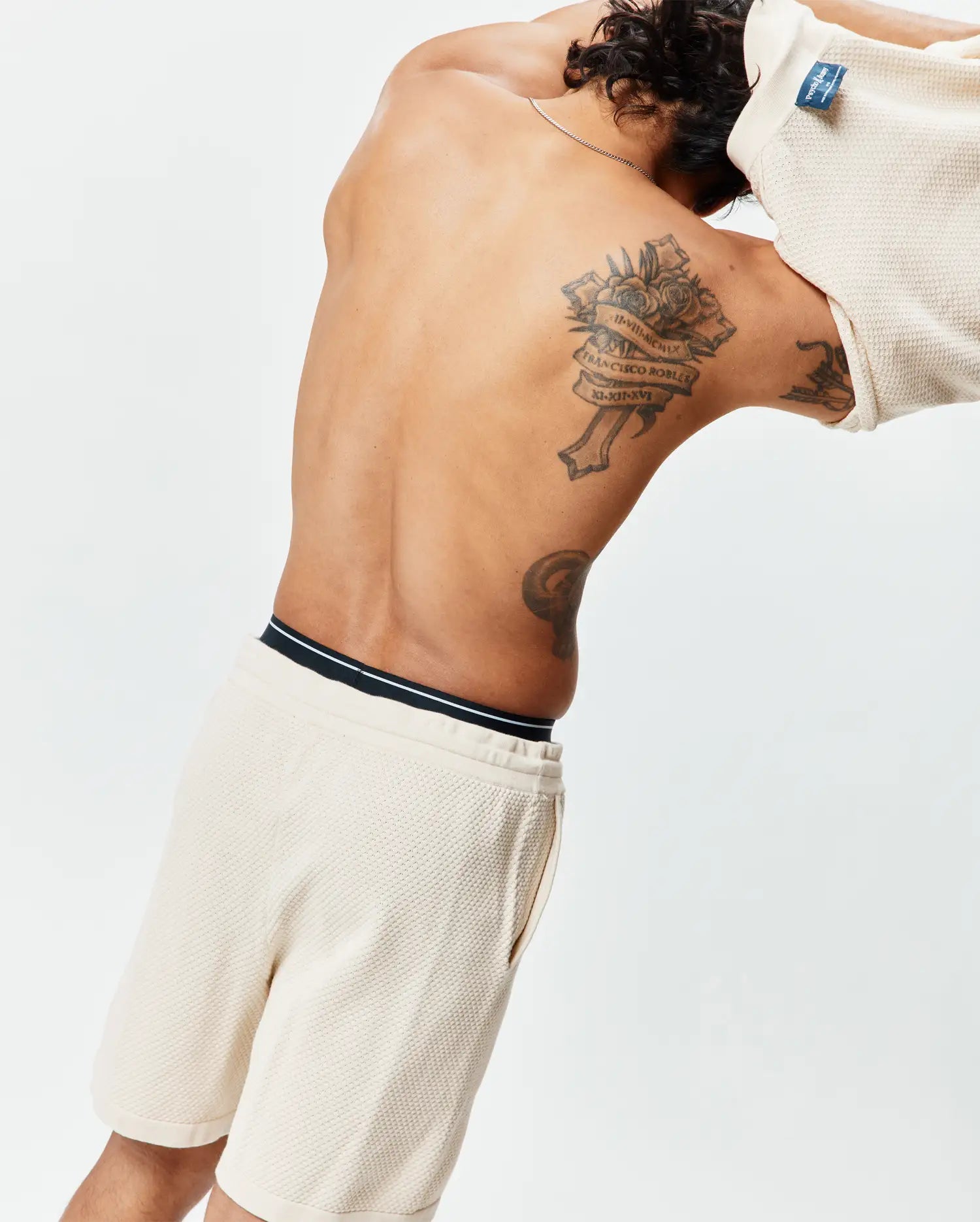 Cream Mens Devon Knit Short, a relaxed waffle knit short with a black and white striped waistband, paired with a matching cream waffle knit top featuring a blue Psycho Bunny tag at the back collar.
