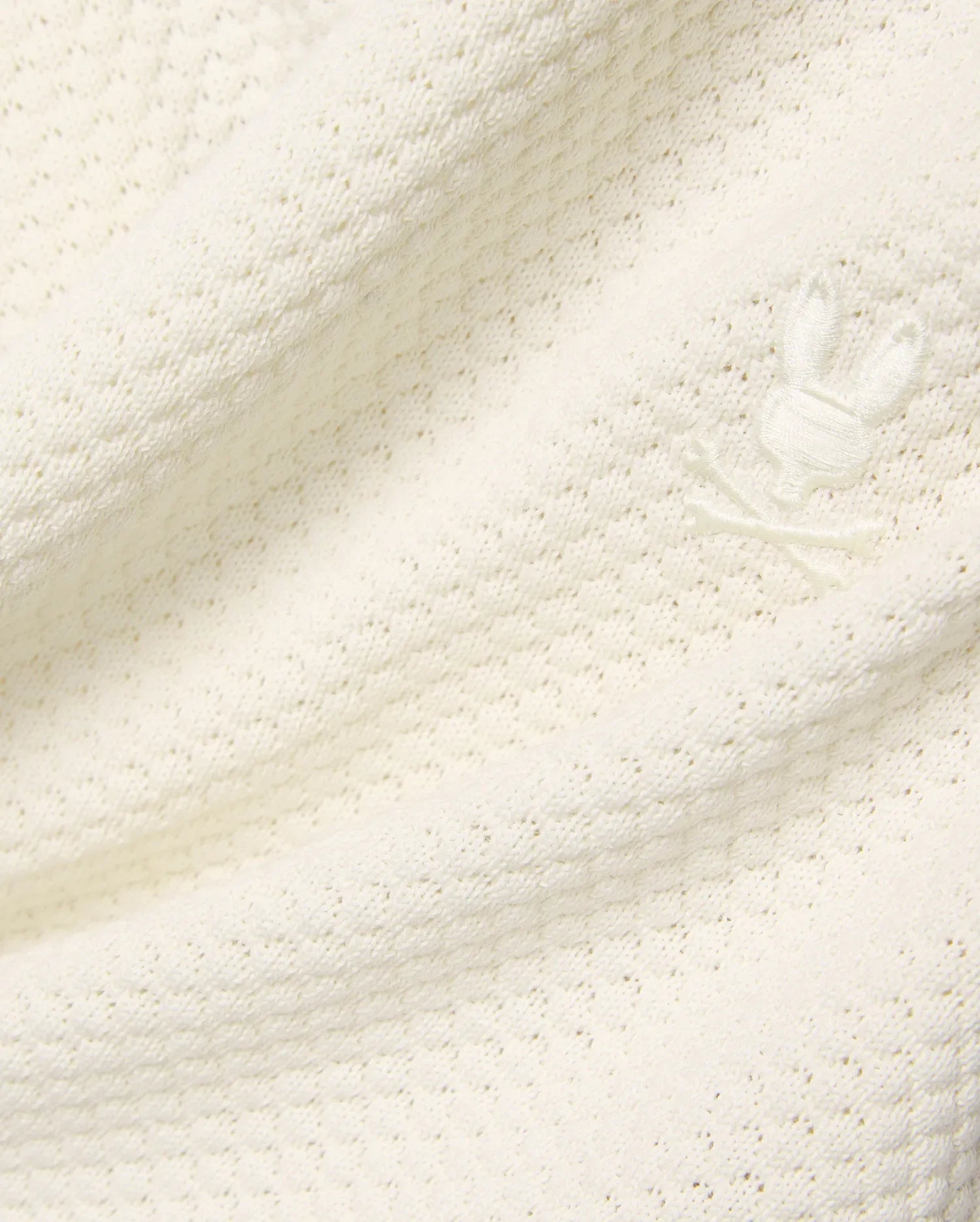 Mens Devon Knit Short in premium cream, featuring a soft, subtly patterned open knit fabric and a small, tone-on-tone embroidered Psycho Bunny skull logo detail.