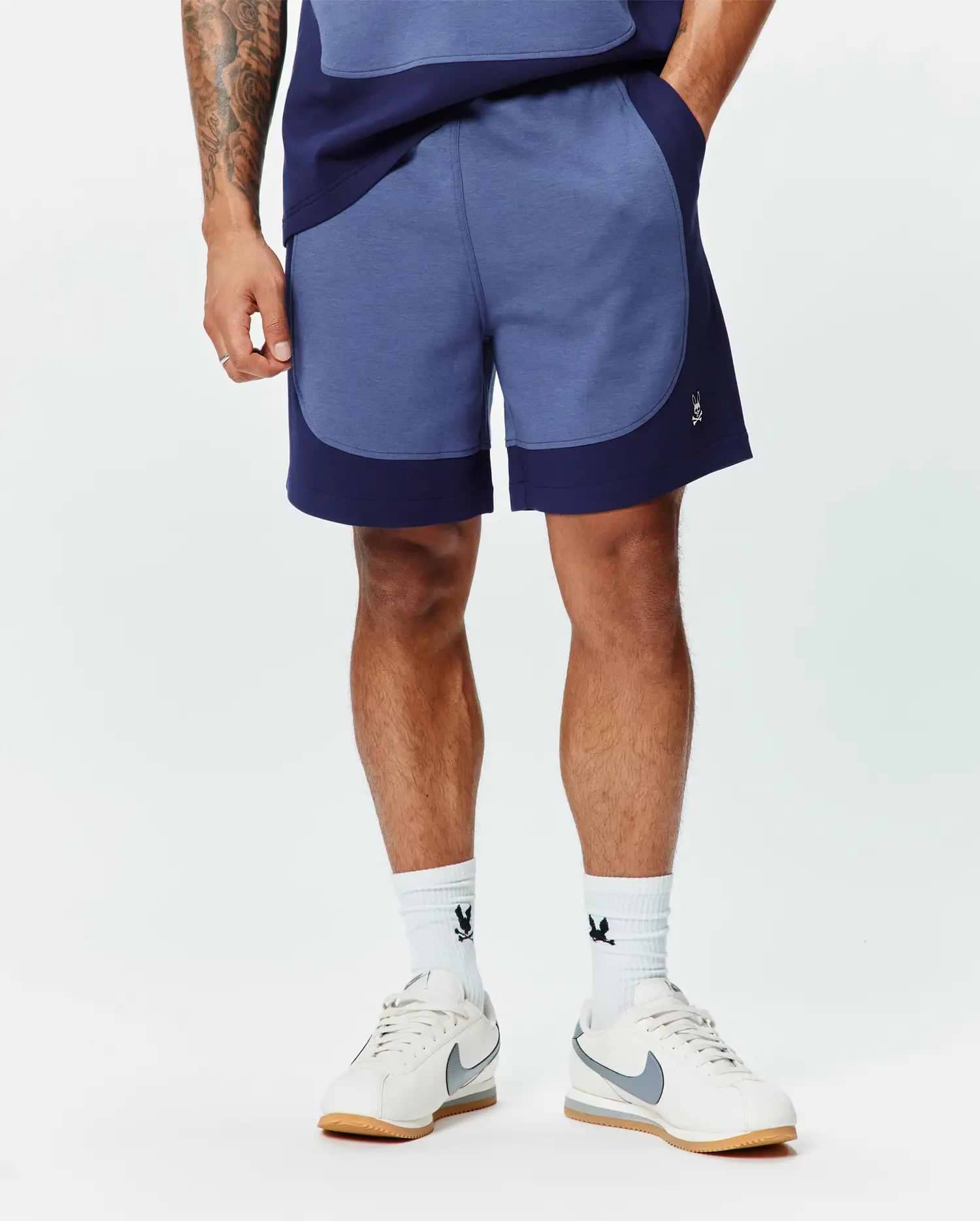 Premium Mens Kelly Short, a relaxed fit heathered blue short with dark navy color-block panels and a small embroidered white Psycho Bunny skull logo on the left leg. (1)