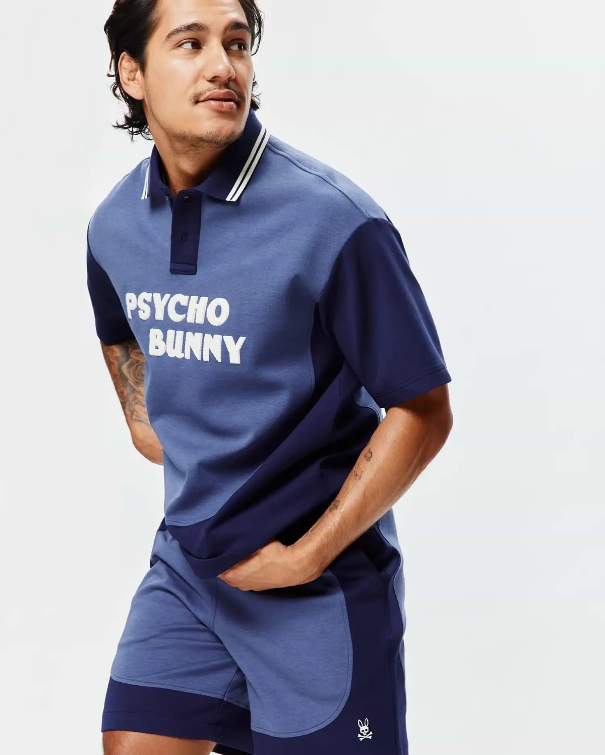 Two-tone blue jersey polo with white PSYCHO BUNNY chest graphic and striped collar, paired with matching color-block Mens Kelly Short featuring an embroidered bunny skull logo. (2)