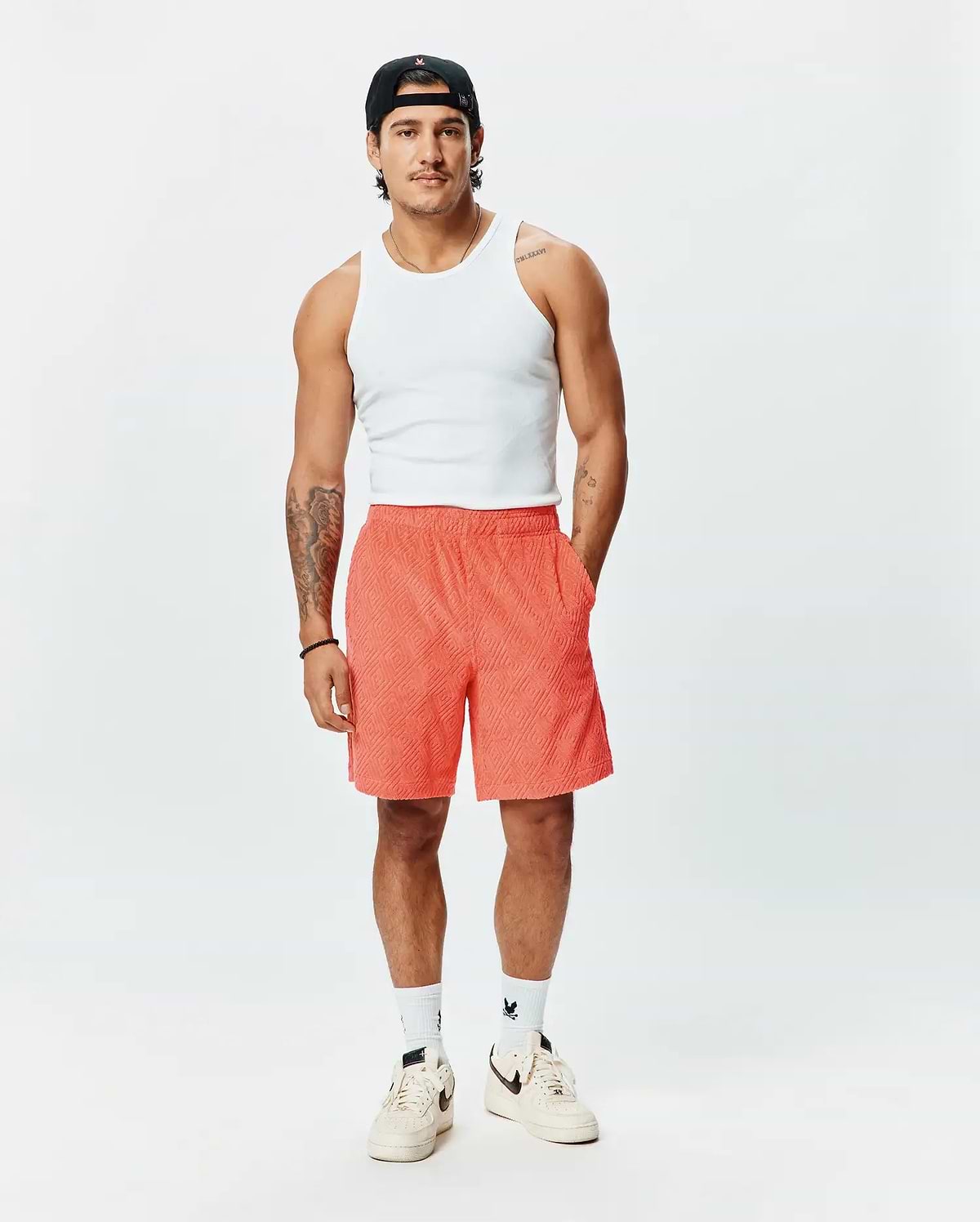 Mens Tristan Short, a premium Psycho Bunny relaxed fit short in vibrant coral, featuring an all-over embossed geometric diamond pattern and practical side pockets.