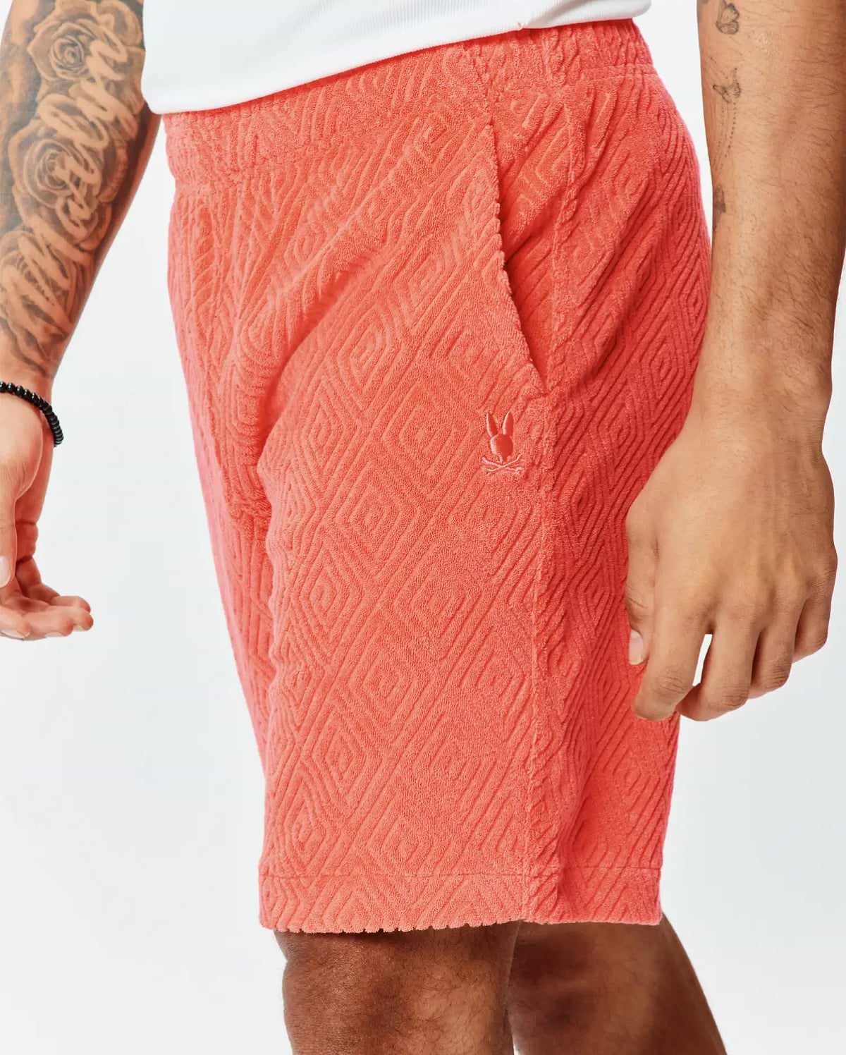 Vibrant coral terry cloth Mens Tristan Short with a relaxed fit, featuring an all-over embossed diamond pattern and a small embroidered Psycho Bunny skull logo on the left thigh.