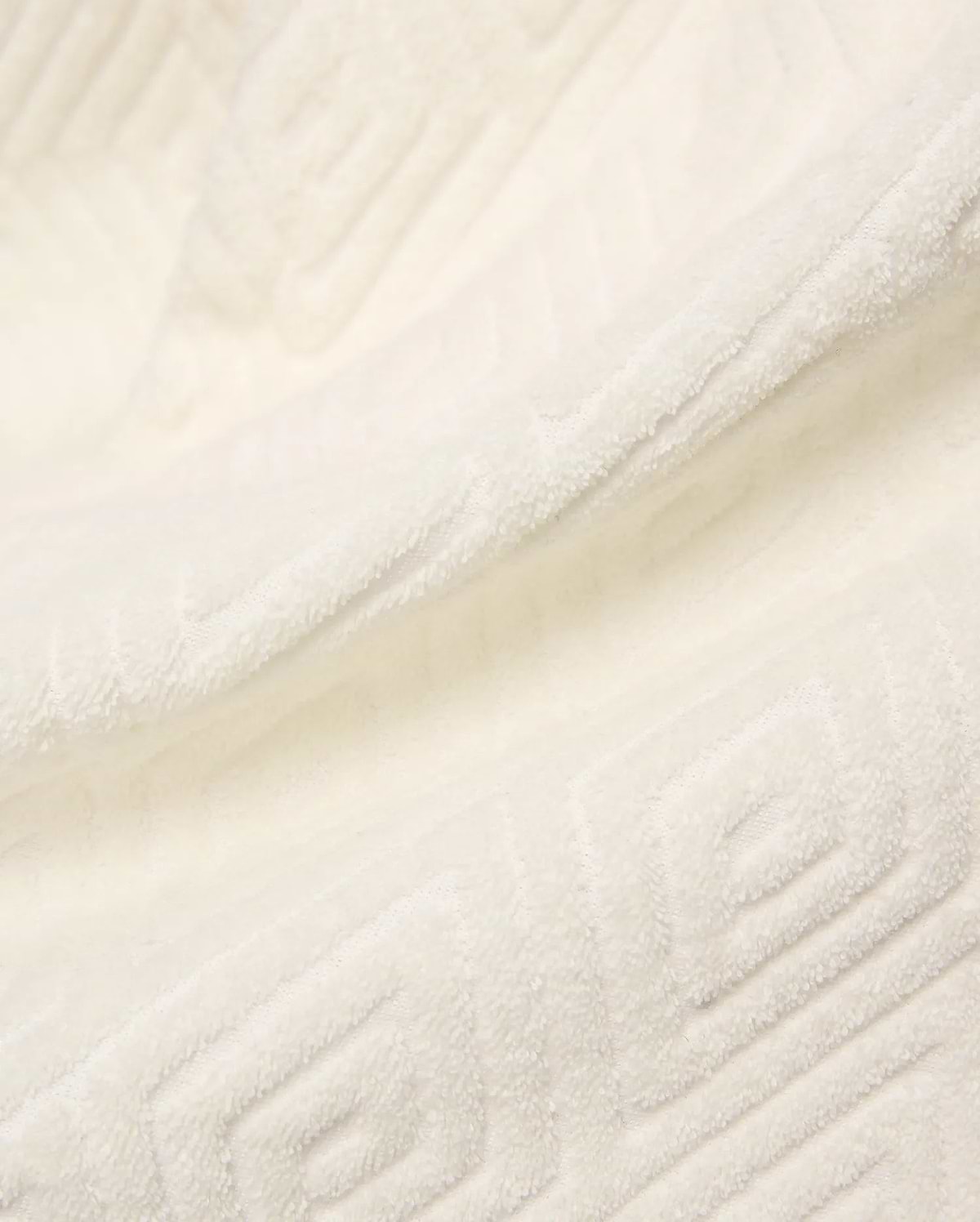 Creamy white Mens Tristan Short crafted from plush, absorbent terry cloth, featuring an intricate, subtly embossed geometric square and spiral pattern throughout the luxurious fabric.