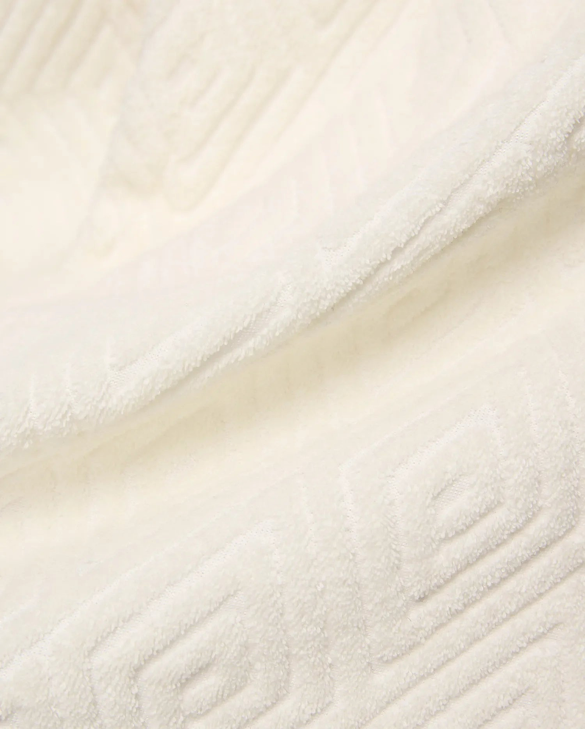 Creamy white Mens Tristan Short crafted from plush, absorbent terry cloth, featuring an intricate, subtly embossed geometric square and spiral pattern throughout the luxurious fabric.
