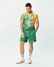 Mens Joshua Soccer Short 7 1/4 in green mesh with white drawstrings and an embroidered Psycho Bunny skull logo on the right leg, paired with a yellow and green graphic t-shirt featuring a large bunny skull print and small sleeve logo. (4)