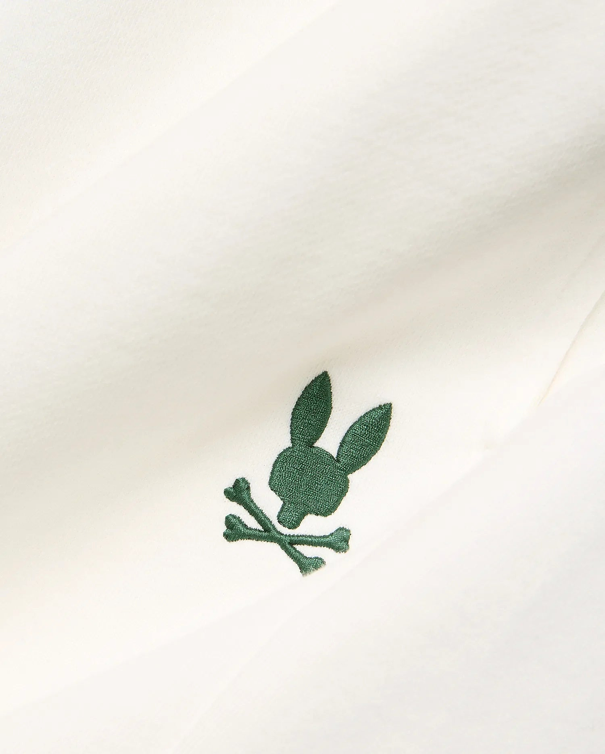 Cream Mens Gabe French Terry Sweatshort, featuring a small, intricately embroidered dark green Psycho Bunny skull and crossbones logo on soft French terry fabric.