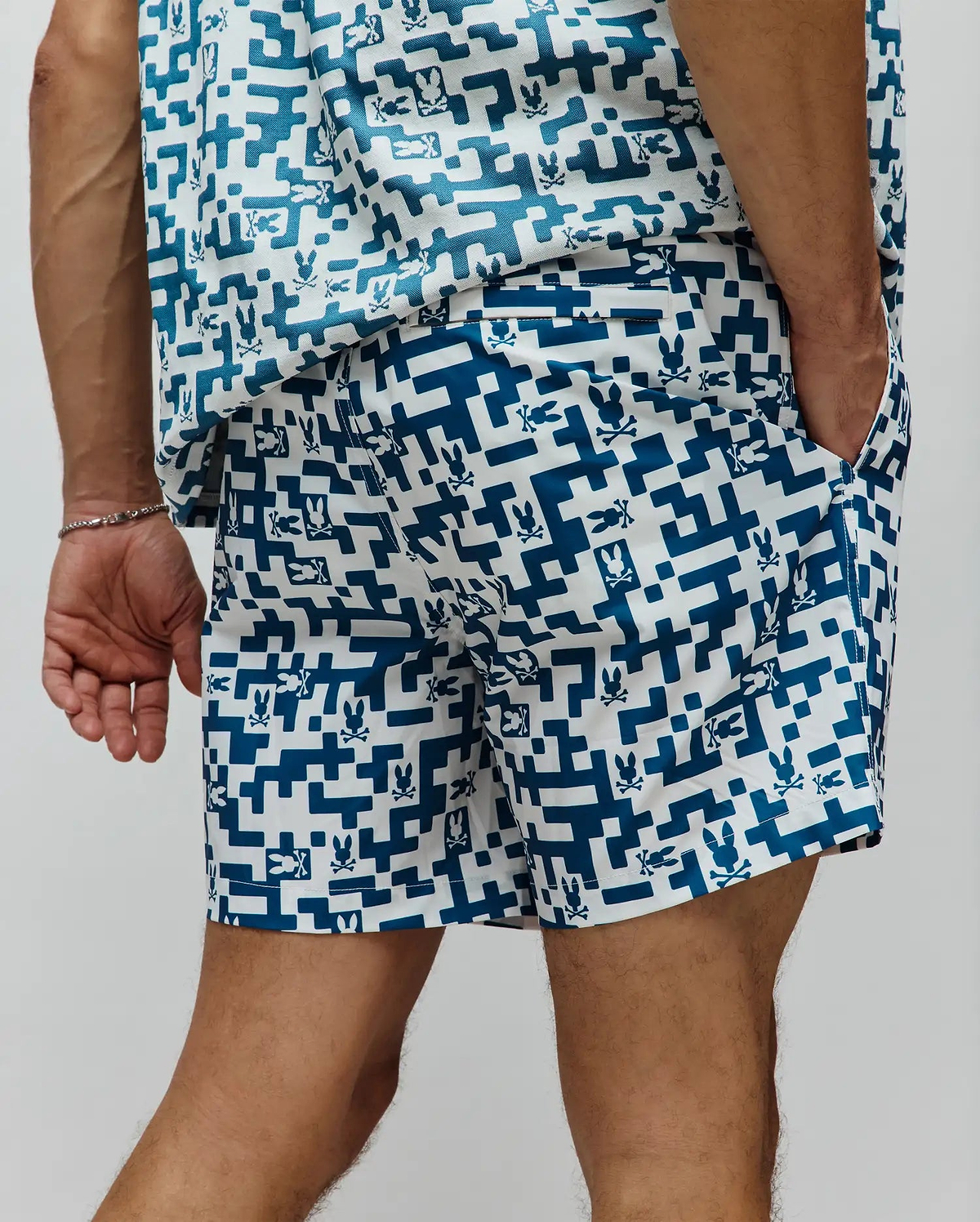 Mens Josh Swim Trunk in white with a deep teal pixelated geometric pattern and repeated small Psycho Bunny skull logos throughout, featuring a classic fit and smooth fabric.