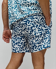 Mens Josh Swim Trunk in white with a deep teal pixelated geometric pattern and repeated small Psycho Bunny skull logos throughout, featuring a classic fit and smooth fabric.