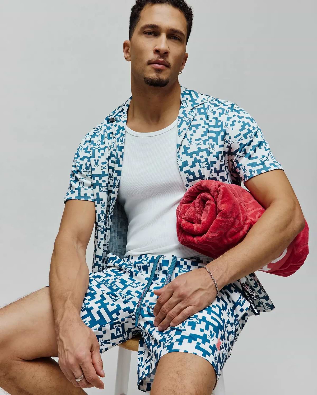 Mens Josh Swim Trunk and matching short-sleeve shirt in white with a teal pixelated pattern featuring small Psycho Bunny skull logos, a relaxed fit resort wear set.