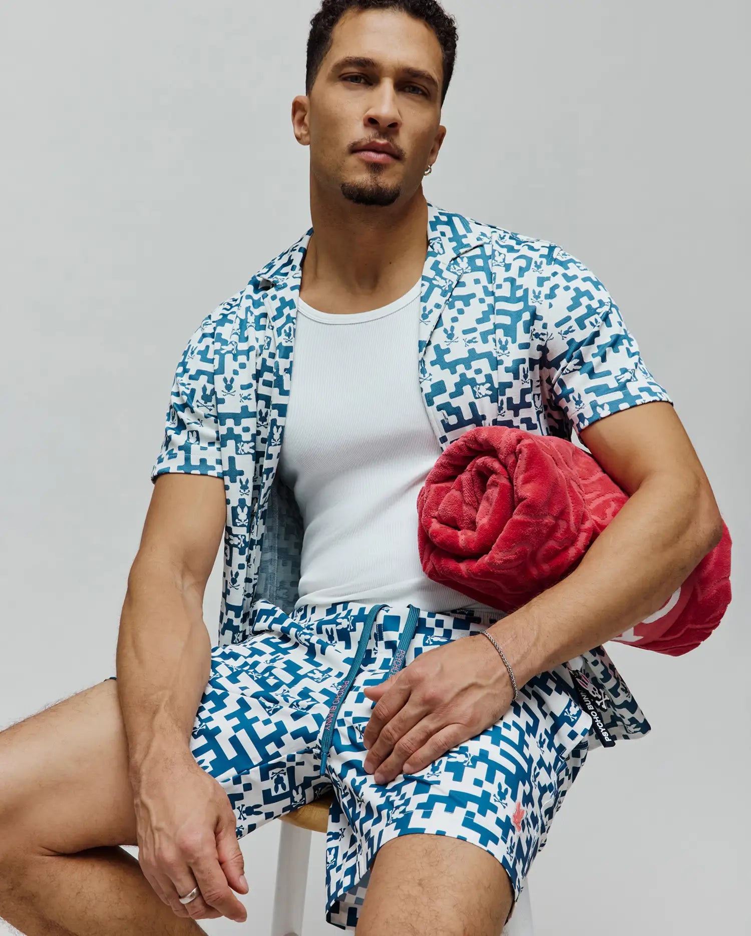 Mens Josh Swim Trunk and matching short-sleeve shirt in white with a teal pixelated pattern featuring small Psycho Bunny skull logos, a relaxed fit resort wear set.