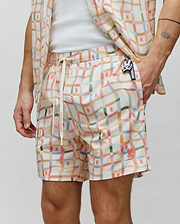 Mens Atlas Swim Trunk in cream with a multi-color wavy plaid pattern featuring small repeated pink Psycho Bunny skull logos, a white drawstring with Psycho Bunny text, and a larger embroidered pink logo on the left leg.