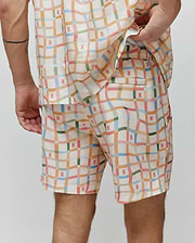 Vibrant pastel plaid Mens Atlas Swim Trunk in cream, featuring numerous small pink Psycho Bunny skull logos, a relaxed fit, and smooth, quick-dry fabric.