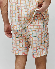 Vibrant pastel plaid Mens Atlas Swim Trunk in cream, featuring numerous small pink Psycho Bunny skull logos, a relaxed fit, and smooth, quick-dry fabric.