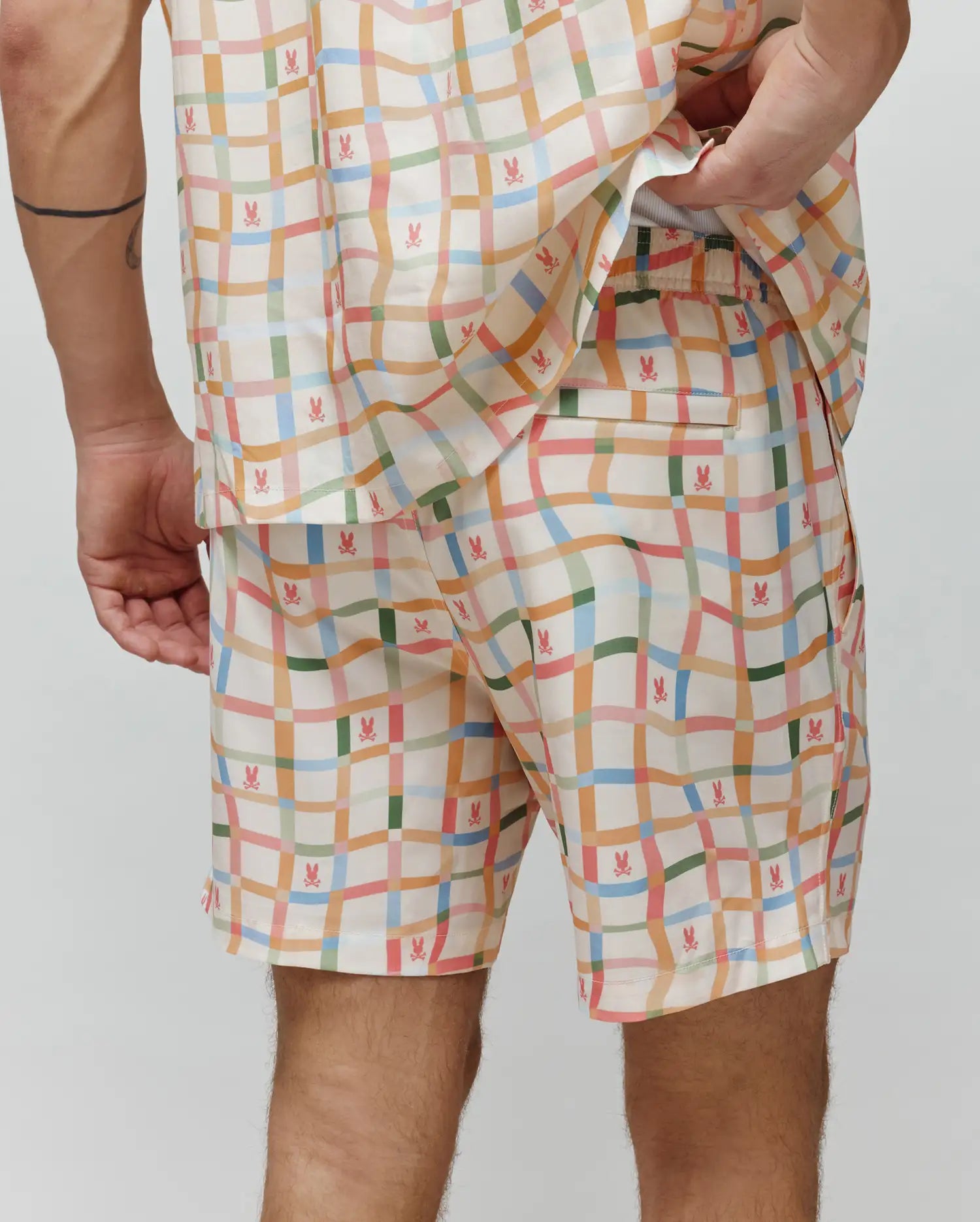 Vibrant pastel plaid Mens Atlas Swim Trunk in cream, featuring numerous small pink Psycho Bunny skull logos, a relaxed fit, and smooth, quick-dry fabric.