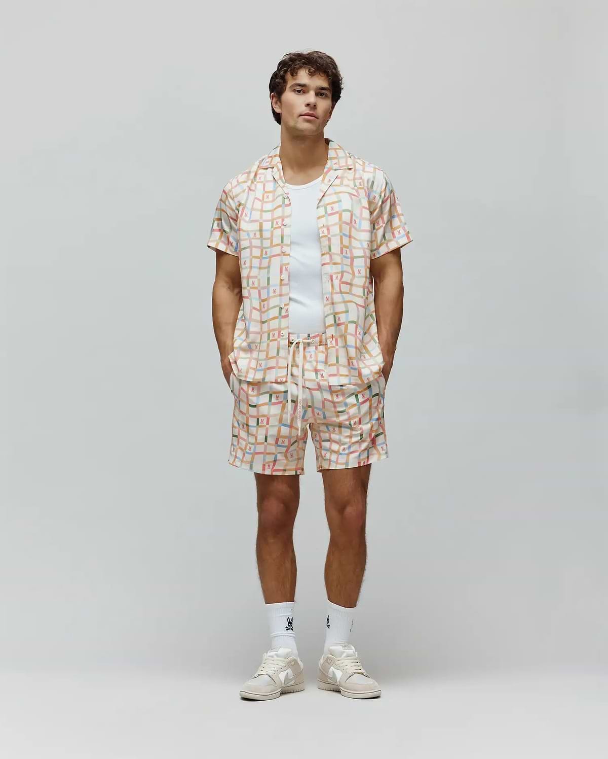 Mens Atlas Swim Trunk and matching camp collar shirt, relaxed fit, in a cream pastel plaid pattern with all-over small Psycho Bunny skull logos and vertical Psycho Bunny text.