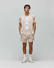 Mens Atlas Swim Trunk and matching camp collar shirt, relaxed fit, in a cream pastel plaid pattern with all-over small Psycho Bunny skull logos and vertical Psycho Bunny text.