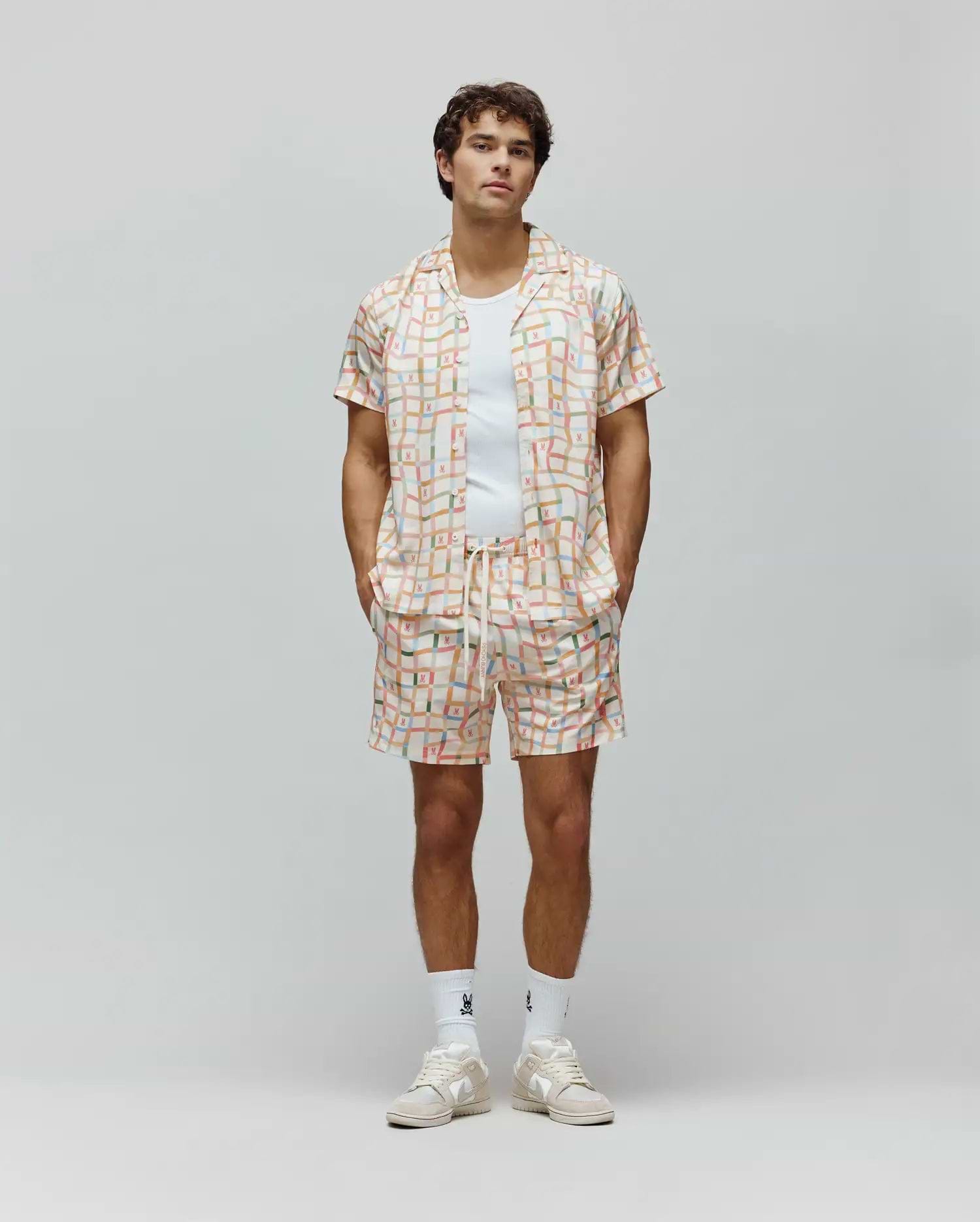 Mens Atlas Swim Trunk and matching camp collar shirt, relaxed fit, in a cream pastel plaid pattern with all-over small Psycho Bunny skull logos and vertical Psycho Bunny text.