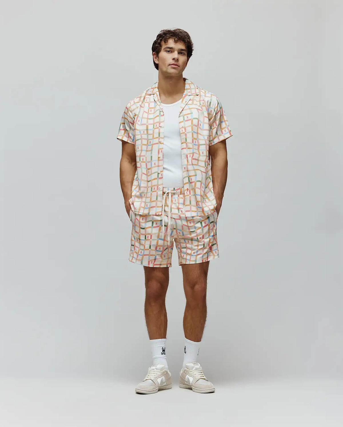 Mens Atlas Swim Trunk and matching camp collar shirt, relaxed fit, in a cream pastel plaid pattern with all-over small Psycho Bunny skull logos and vertical Psycho Bunny text.