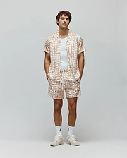 Mens Atlas Swim Trunk and matching camp collar shirt, relaxed fit, in a cream pastel plaid pattern with all-over small Psycho Bunny skull logos and vertical Psycho Bunny text.