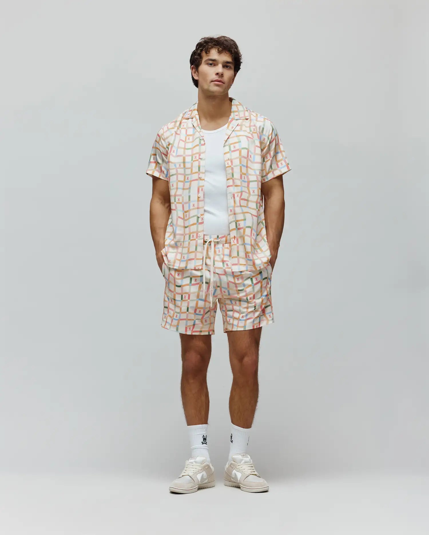 Mens Atlas Swim Trunk and matching camp collar shirt, relaxed fit, in a cream pastel plaid pattern with all-over small Psycho Bunny skull logos and vertical Psycho Bunny text.
